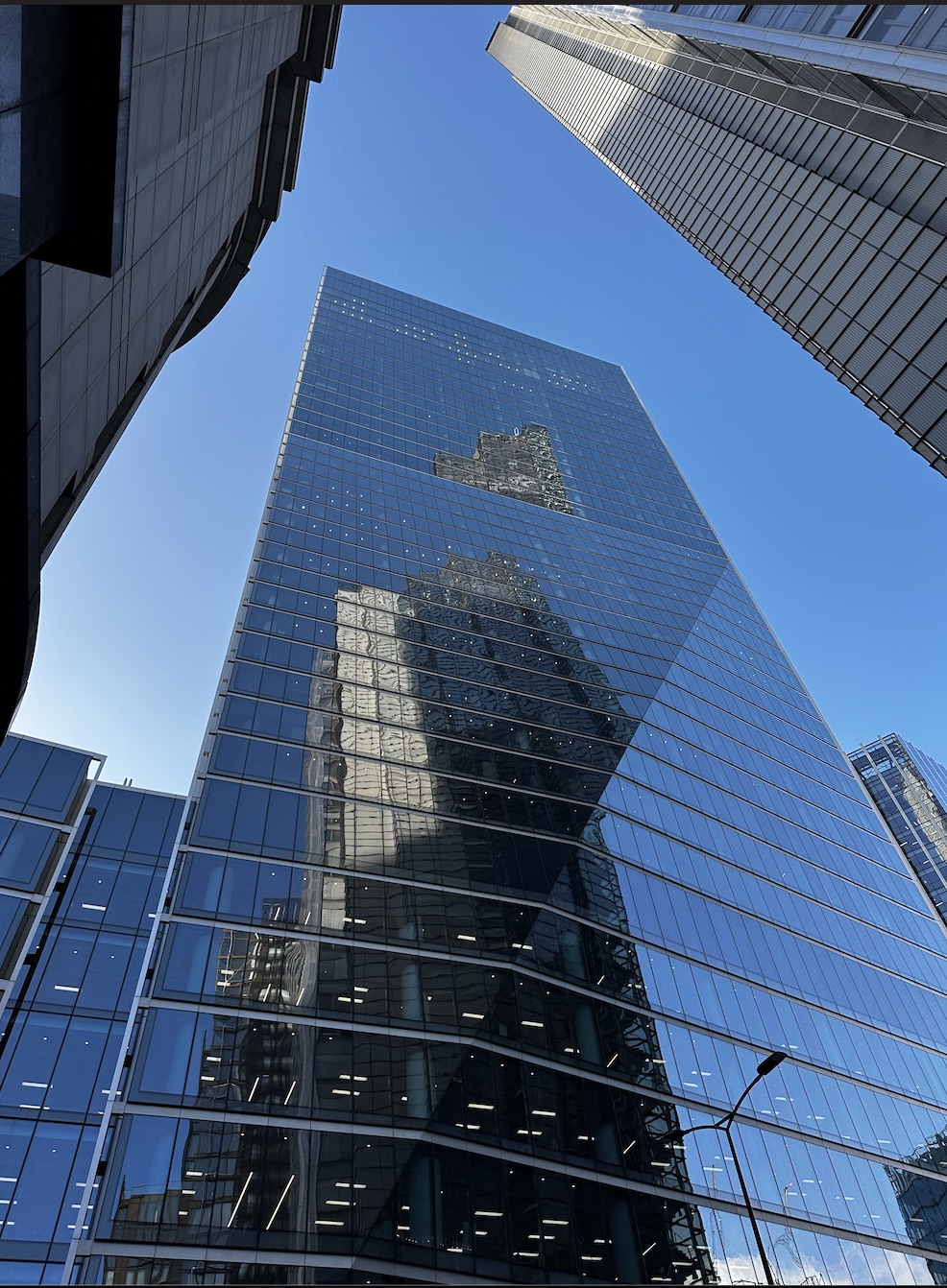 Looking up the mirrored glass face of a skyscraper against a blue sky