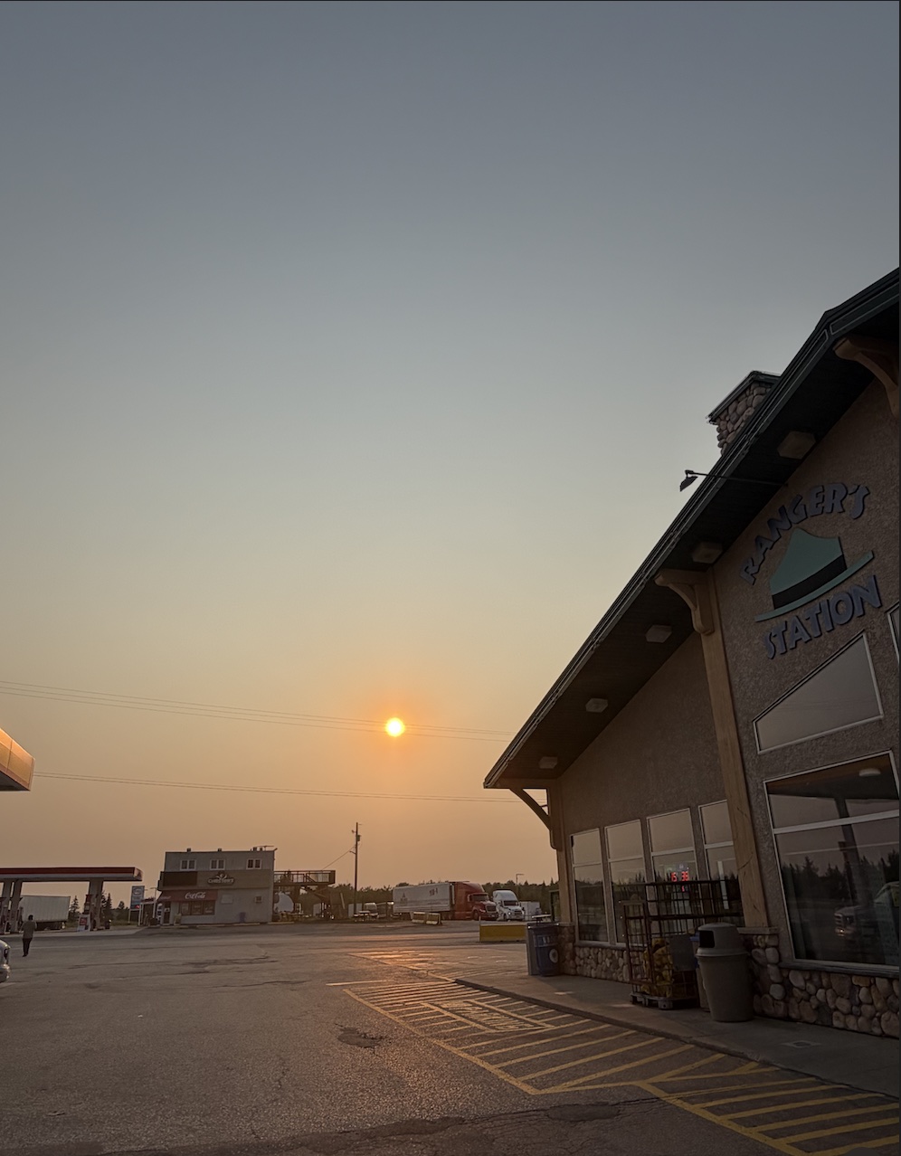 A smoky orange sun setting over a roadside gas station and a log-style building